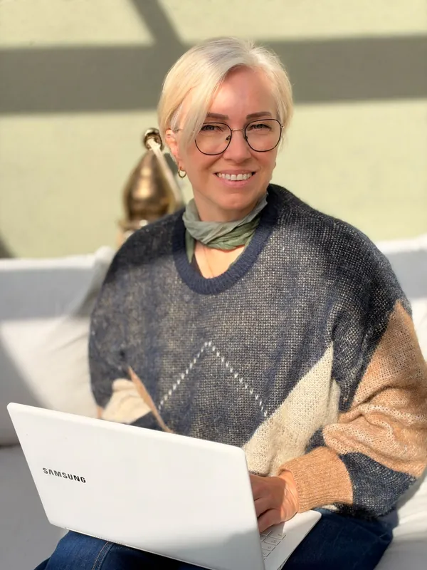 Jutta Gradwohl sitzt lächelnd mit Brille und Laptop auf einem hellen Sofa